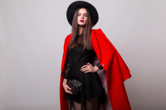 Fashionable woman in  red coat and black hat posing in studio, looking at camera. cold season. Autumn or winter look.